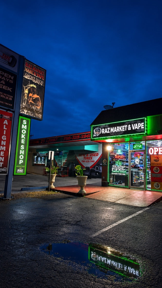 RAZ storefront at dusk with green illuminated signage reflected in the pavement